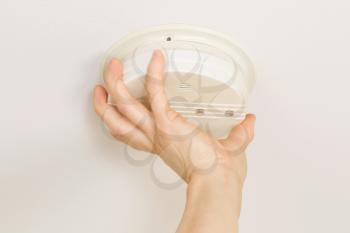 Horizontal photo of female hands putting home smoke detector together with white ceiling in background