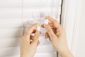 Photo of female hands adjusting strings on windows blinds