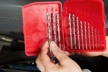 Horizontal photo of female hand holding drill bit with toolbox in background 