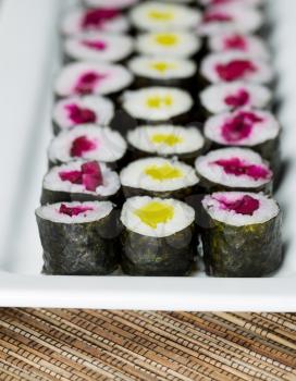 Vertical front view photo of pickled sushi hand roll on long white plate with natural bamboo mat underneath