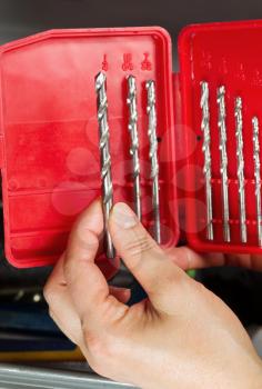 Vertical photo of female hand holding drill bit with toolbox in background 