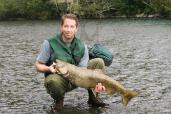 Horizontal photo mature man holding large king salmon while wading in river 