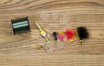 Horizontal top view photo of fishing flies, spoon, float and spool of line on faded wood