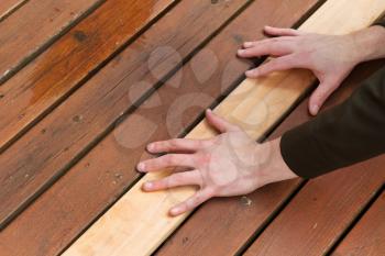 Horizontal photo of male hands putting in a single new cedar wooden board next to fading wood on outdoor deck 
