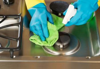 Closeup horizontal image of hands wearing rubber gloves while cleaning stove top range with spray bottle and microfiber rag