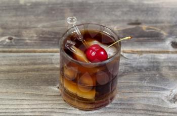 Horizontal top view of a rum and cola with large red cherry and ice in glass position on rustic wood 