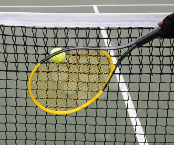 Tennis ball goes into net with racket and players hand behind ball