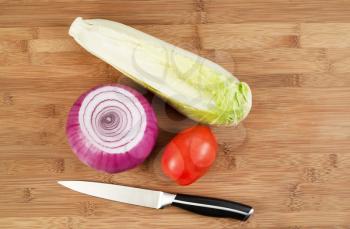 Closeup horizontal top view photo of fresh whole red onion, lettuce and tomato with kitchen knife beside and natural bamboo wood underneath