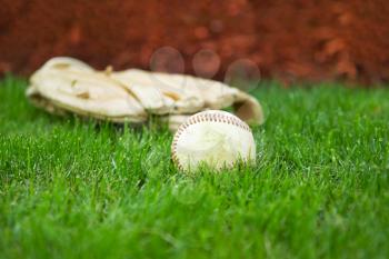 Closeup horizontal photo of old baseball with glove in background on natural grass field 