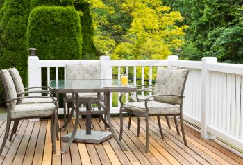 Closeup horizontal photo of outdoor furniture on open cedar patio with seasonal trees in full bloom in background 
