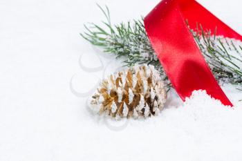 Closeup front view of golden pine cone with red ribbon and fir branch covered in snow 