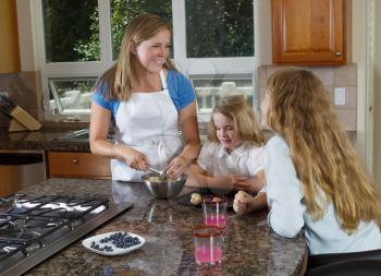 Front view of mother making cookie dough with her daughters watching while in the kitchen