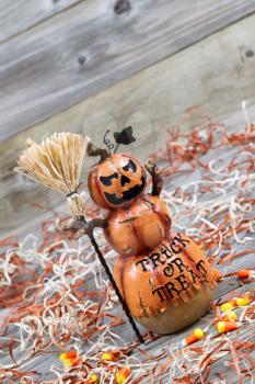 Vertical angled image of a scary orange pumpkin figure holding straw broom placed on rustic wooden boards 

