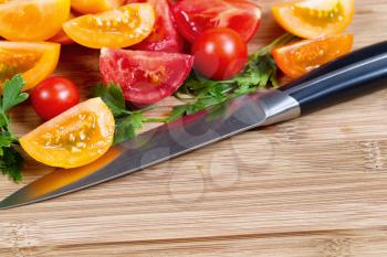 Closeup horizontal image of kitchen knife and slice tomatoes and parsley on natural bamboo cutting board