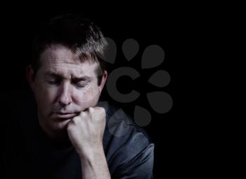 Front view close up of mature man with his eyes closed and chin in hand displaying depression on black background  