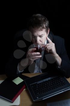 Vertical image of business man, drinking alcohol, working late with black background 
