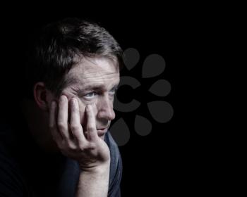 Closeup side view of mature man with his chin in hand displaying depression on black background  

