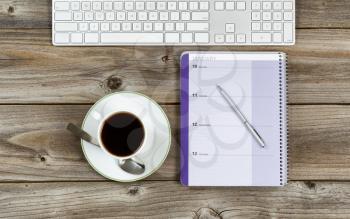 Top view of business office objects consisting of calendar, pen, computer keyboard and cup of coffee on rustic wooden desktop 