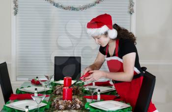 Young teenage girl, dressed in Santa outfit, lighting candle for holiday party at the dining room table  