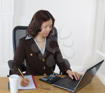 Mature business woman preparing to take notes while looking at the computer monitor.  Background is white walls. 