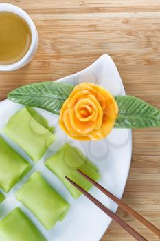 Close up top view vertical image of Chinese Durian fruit dessert rice cakes, yellow decoration rose, and green tea on natural bamboo background