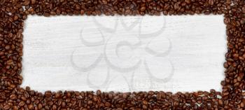 Freshly roasted coffee beans, forming even border, on white wooden table. 