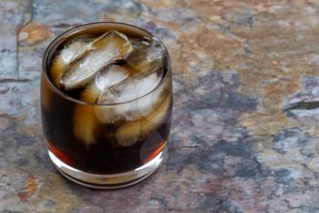 Close up of a Fresh cola drink with real ice on natural rustic slate background. Focus on front part lip of glass.