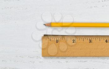 Close up of a traditional wooden ruler, with metal edge, and yellow pencil on white boards