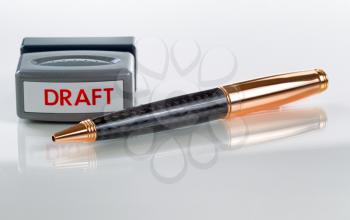 Elegant business pen and draft stamp, focus on part of pen front and stamper, in background on glass with white background  