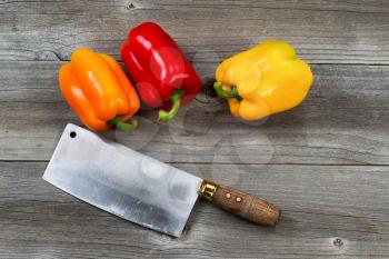 Top view angle of three fresh bell peppers and old butcher knife on aged wooded boards