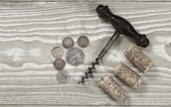Vintage concept of antique corkscrew with three used corks, old coins on rustic wooden boards. Top view angled shot in horizontal format.

