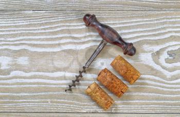 Antique corkscrew with three used corks on rustic wooden boards. Top view angled shot in horizontal format with copy space. 