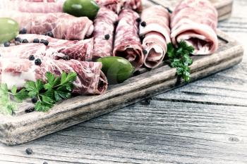 Vintage concept of various cold meats on serving board with ham, pork, beef, parsley, and olives on rustic wood. Focus on side part of serving board and first row of meat. 
