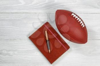 Image of executive notepad, pen and American football on white rustic wood. Playbook concept for game plan.