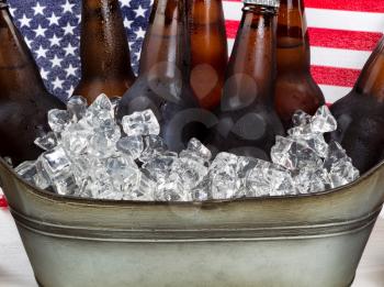Close up of cold beer and ice in steel tub with American flag in background. Fourth of July holiday concept. 