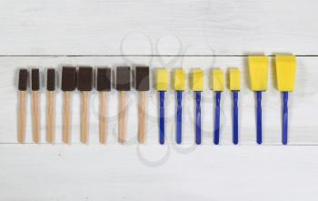 High angled view of brand new paint applicators organized on white wood. Layout in horizontal format.