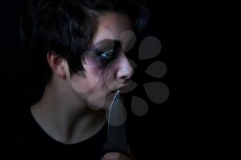 Teen girl masked in scary makeup with combat knife on black background. 