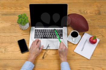 High angled view of male hand holding pencil, point at screen, while typing on computer keyboard. Game plan concept with football in background. 