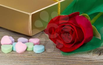 Close up of a red rose, wrapped in soft green paper, heart shaped candy and golden gift box on rustic wood. Valentines day concept. 