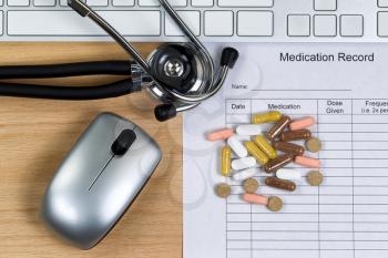 Patient medication record form with stethoscope, pills, computer keyboard and mouse on wooden desktop. Mouse and keyboard are nonfunctional no name brand items for display on desktops.  