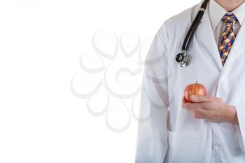 Partial front view of doctor holding apple in hand while wearing jacket with stethoscope on white background.  