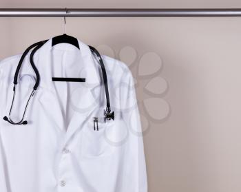 Medical Doctor Consultation white coat with pens and stethoscope hanging on rack with off white wall in background. Horizontal layout with copy space. 