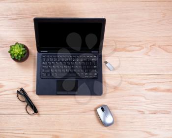 Overhead view of a clean desk consisting of laptop, baby plant, mouse, thumb drive, and reading glasses. 