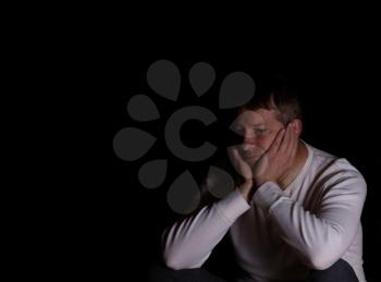 Depressed mature man, looking away from camera, holding his head in both hands. Dark background with copy space available. 