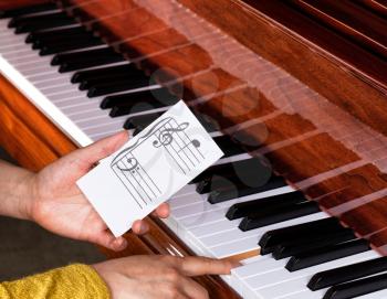 Close up of female hands holding music key card to show exact location on piano keyboard. Select focus on music key card. 