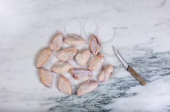 Overhead view of raw chicken wings and kitchen knife of natural marble stone countertop