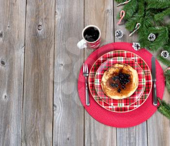 Overhead view of a festive Christmas breakfast meal and coffee with evergreen branches on top of rustic wood. 