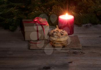Fresh cookies, neatly tied with string, along with warmness of glowing red candle and gift in background for holiday concept. 