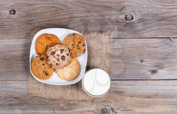 Overhead view of a variety of freshly baked cookies on a napkin with a glass milk. 
