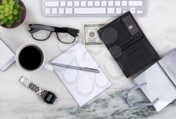 Overhead view of office desktop with computer keyboard, cell phone, shopping bag, wallet, money, pen, paper, reading glasses, coffee and plant on marble surface. Shopping on line concept. 